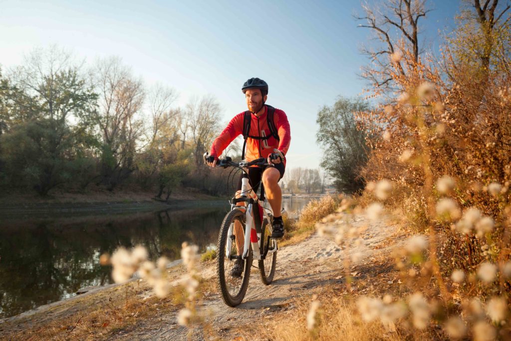 Happy young man enjoying late afternoon mountain bike ride by the river on a clear autumn day