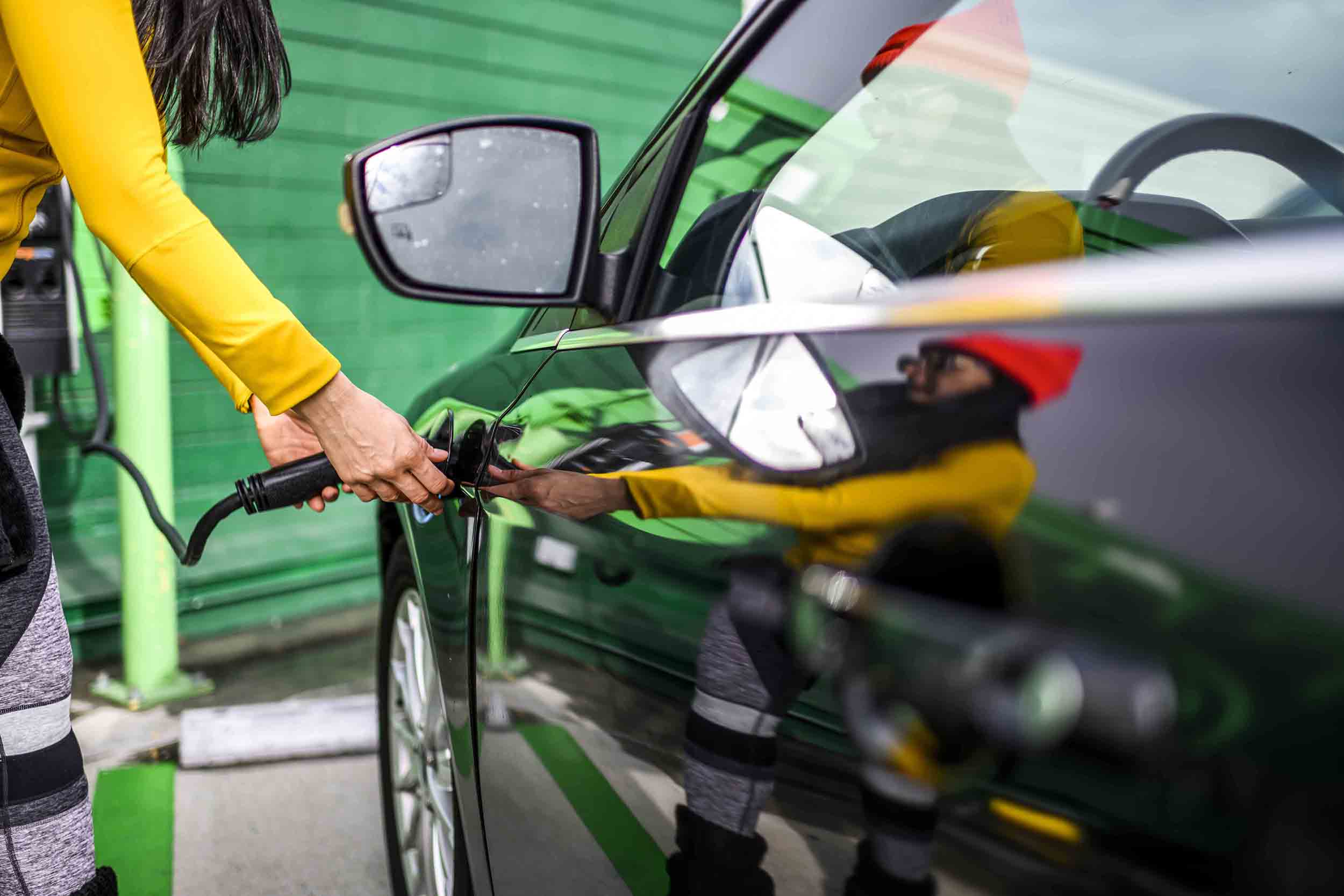 Woman plugs charging cable into electric vehicle