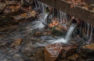 Overflow from an autumn rain drains from pipes next to a stream