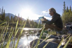 man reads map on mountainous riverbank at sunrise