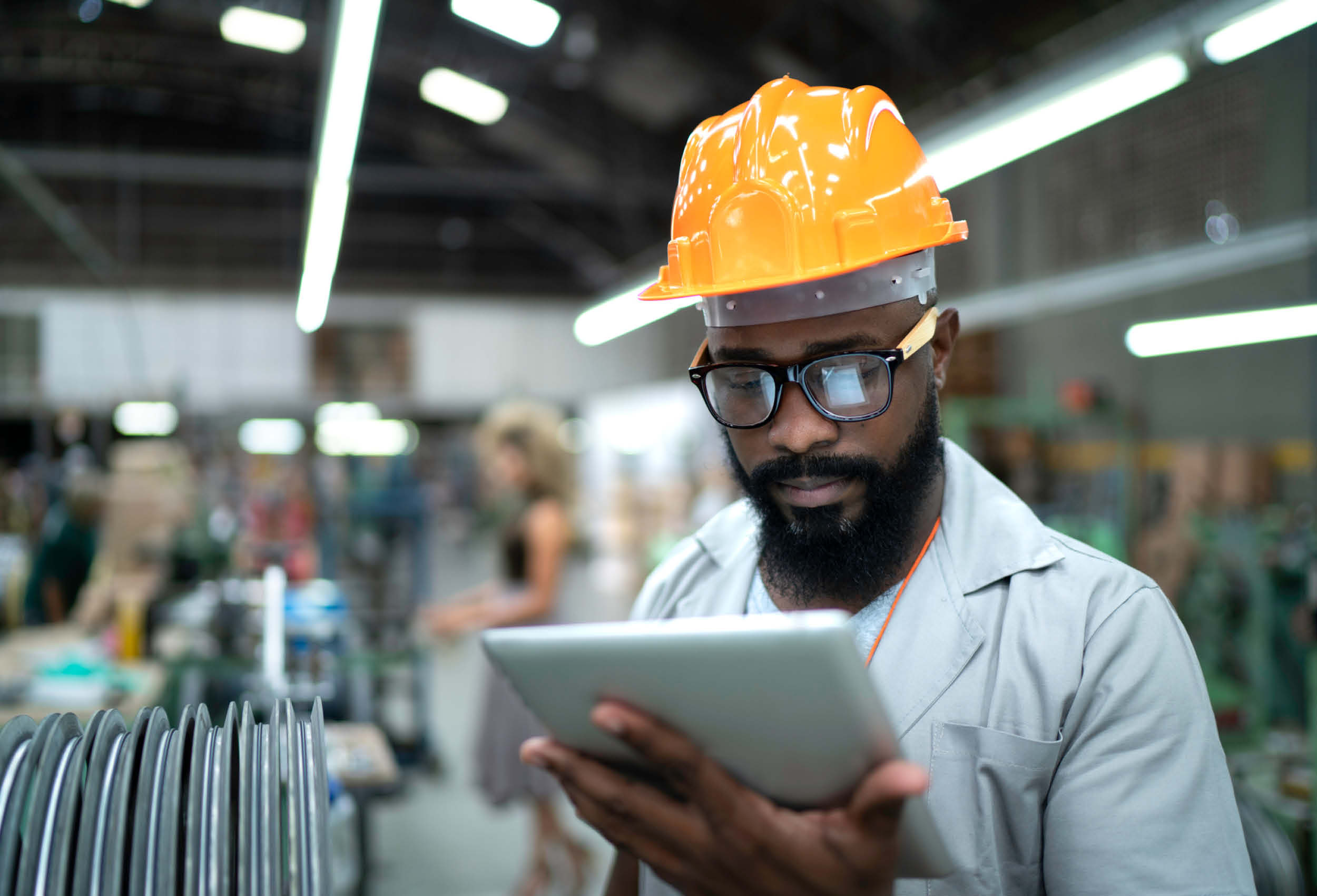 Engineer wearing hardhat uses tablet in factory.