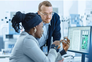 Supervisor talks with employee in front of computer.