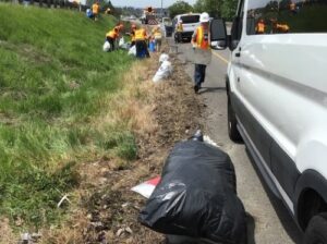 A team of people picking up litter off the side of the road.