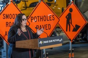 Woman giving a speech in front of road work signs.