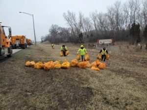 People picking up bags of trash off the side of the road.